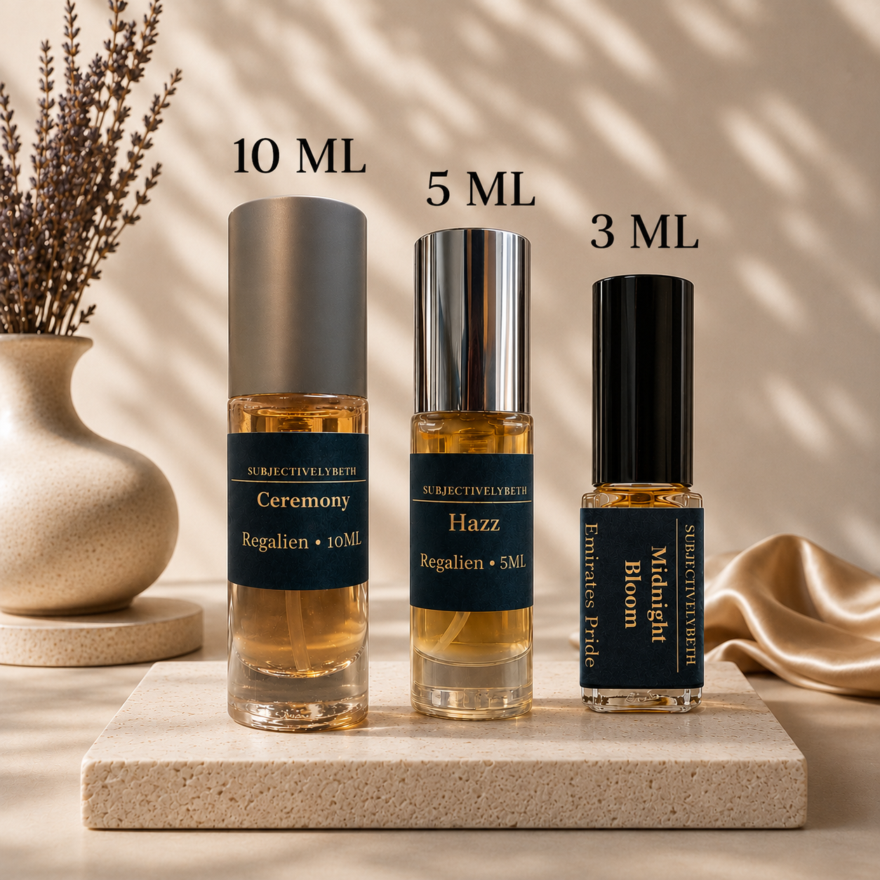 Three perfume bottles with labels on a marble surface with a vase and fabric in the background.